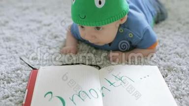 三个月的<strong>宝宝</strong>戴着一顶绿色的龙形<strong>帽子</strong>，躺在地上的笔记本上。
