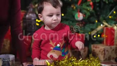 圣诞树上的孩子。 有兴趣的宝宝玩礼盒.. 孩子看到一个金色的金属圈，推了推她的脚