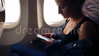 一个年轻的女孩坐飞机，看智能手机上的照片。