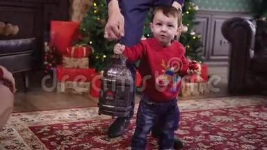 <strong>父亲帮助</strong>他的小儿子手里拿着一盏古老的古董灯在圣诞树的背景下