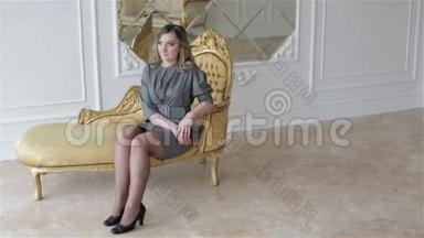 一个穿灰色商务礼服的女人坐在一张金色的老式沙发上。