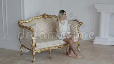 一个年轻漂亮的金发女孩坐在一张<strong>老式沙发</strong>上。