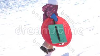 冬天散步的孩子。 一个女孩骑在塑料板上的雪滑板上。