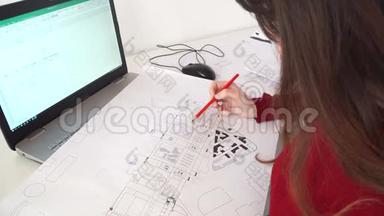 女工程师坐在她办公室的办公桌前，在笔记本电脑上打字，在她的办公桌上放蓝图