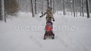 年轻快乐的母亲在冬天的森林里的小路上，和她的小女儿一起沿着红色的雪橇<strong>前行</strong>