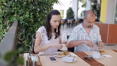 年轻夫妇在户外咖啡馆的一张<strong>桌子</strong>上吃<strong>早餐</strong>和聊天