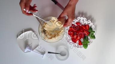 一个女人用奶油填充烹饪注射器。 <strong>碟子</strong>旁边是一个草莓。