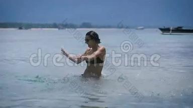 穿着黑色比基尼的布鲁内蒂在巴厘岛海滩上和水一起跳舞和飞溅。 年轻女孩