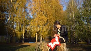 一个穿着皮夹克的年轻女人在公园里编织一条格子呢。