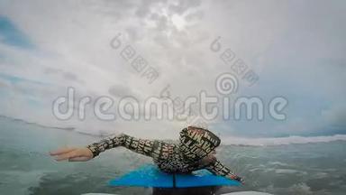 年轻人划桨，双手躺在冲浪板上，然后站起来，在海洋中乘风破浪。 积极接待游客