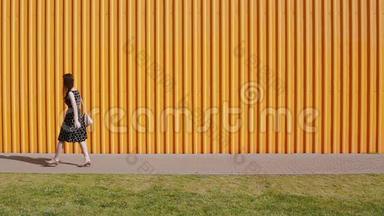 在一个阳光明媚的日子里，穿着黑白裙子的美丽年轻女子沿着黄色的墙走了一半