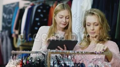 两个年轻女子在一家服装店购物。 好好享受你的平板电脑，看看目录和商店里的东西