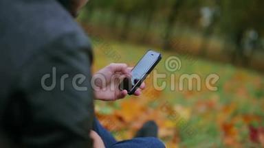 在秋天的公园里，坐在草地上的人用智能手机触摸板输入短信