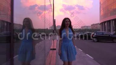 苗条的黑发女孩，穿着蓝色连衣裙，在<strong>粉红</strong>色日落天空的街道上散步，4K<strong>视频</strong>