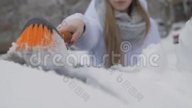 年轻漂亮的女孩用刷子擦车上的雪