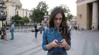 布鲁内特漂亮的年轻女子穿着牛仔裙走在街上。 她用她的智能手机。 慢莫，稳定射击