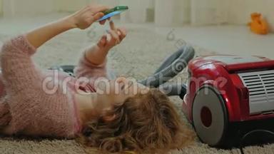 快乐的年轻女子或家庭主妇，带着吸尘器，躺在地板上，用电话，玩得开心，玩得开心