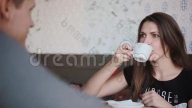 年轻漂亮的女人和一个男人坐在咖啡馆里，喝着一杯咖啡。 他们玩得开心，笑得开心