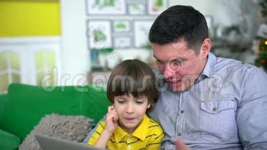 父子使用笔记本电脑。 英俊的<strong>父亲</strong>看着电脑，他<strong>和</strong>非常可爱的<strong>儿子在家里</strong>的沙发上背景