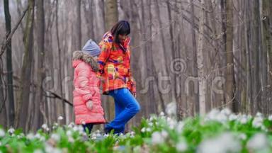 母亲和女儿正在阳光明媚的阳光下，穿过满是雪花的春天森林