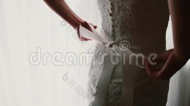 年轻新娘的近景在她的婚纱上<strong>鞠躬</strong>。 女人站在窗边准备仪式