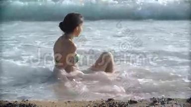 年轻漂亮的晒黑女人穿着比基尼坐在海滩上。 女孩放松了，海浪