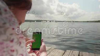 女孩躺在河上的木墩上看着智能手机的绿色屏幕