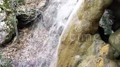 在长满青苔的石质河床上流动的小山河上瀑布的侧景。 春天纯净的淡水