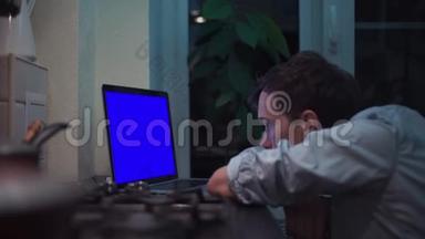 男人在灶台附近的厨房里看着蓝键笔记本电脑