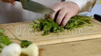 厨刀的手在大厨房里，一根新鲜的绿色欧芹放在一棵树上的砧板上