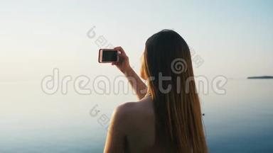 美丽的年轻女子在<strong>海边</strong>海滩的日落时用智能手机<strong>拍照</strong>度假。 慢动作