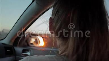 风吹过女孩的剪影和头发在车里。 少女在车里听音乐。 <strong>日</strong>落