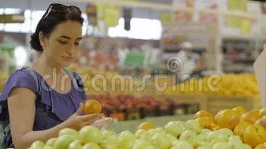 漂亮的年轻女人，深色头发的女人在超市里选择水果-新鲜的橙色。 购物和人的概念。 股票
