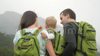 一个年轻的旅人家庭，带着一个回头看群山。 每个人都有相同的绿色背包。