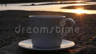 一杯芬芳的咖啡矗立在河边的一块岩石上，可以看到金色的日落和水上的眩光。 <strong>高清高清</strong>