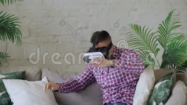 年轻的快乐男子戴着虚拟现实耳机，玩360VR电子游戏，坐在客厅的沙发上。