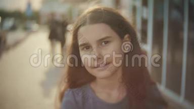 城市中一个小女孩的肖像，人群散步，人们慢动作视频。 女孩青少年的阳光肖像。 城市