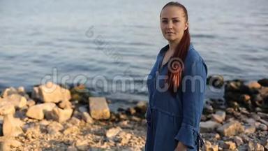 年轻美丽的白人中年妇女，红色头发，穿着蓝色牛仔裙，站在海边。