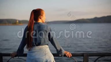 年轻美丽的白人中年妇女，红色头发，穿着蓝色牛仔裙，站在海边。