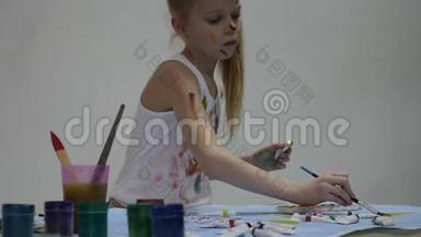 小女生。 可爱的小女孩画家在桌子上画画，在她的衣服上画画。 慢动作