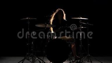 女孩是踢鼓，演奏精力充沛的音乐。 黑色背景。 剪影