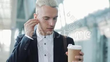 年轻有魅力的男人走在街上，拿着咖啡，听着耳机听着音乐，走来走去