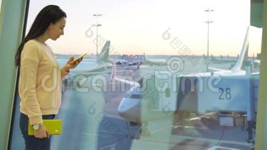 航空公司乘客在机场休息室等待航班飞机。 白种人女人在大窗户附近用手机说话