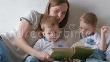 家庭妈妈和两个双胞胎兄弟蹒跚学步的孩子在床上看书。 家庭阅读时间。