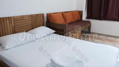 一间带白色<strong>双人床</strong>的<strong>酒店</strong>客房，带橙色靠垫和巧克力窗帘的棕色沙发