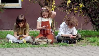 两个兄弟和一个妹妹坐在草地上使用智能手机。 在社交网络中社交。 网络依赖