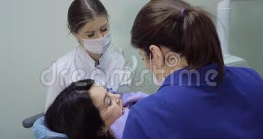病人坐在<strong>牙医</strong>椅上做检查，<strong>牙医</strong>带着镜子检查牙齿，护士坐在旁边