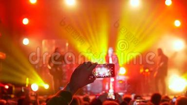 在聚光灯下的音乐会晚会上，粉丝在手机上拍摄视频和照片