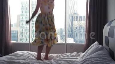 穿着连衣裙的年轻快乐女子跳上酒店的床。慢动作。3840x2160