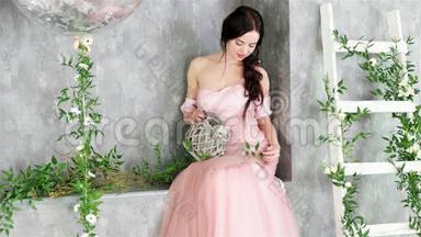 穿着粉红色<strong>长裙</strong>的迷人<strong>女士</strong>坐在植物工作室装饰的灰色角落里